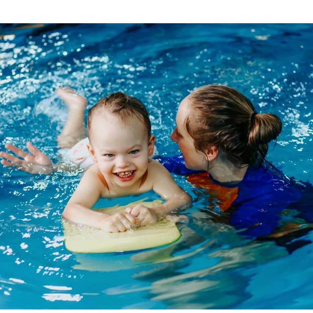 A baby is swimming in the water with an adult.