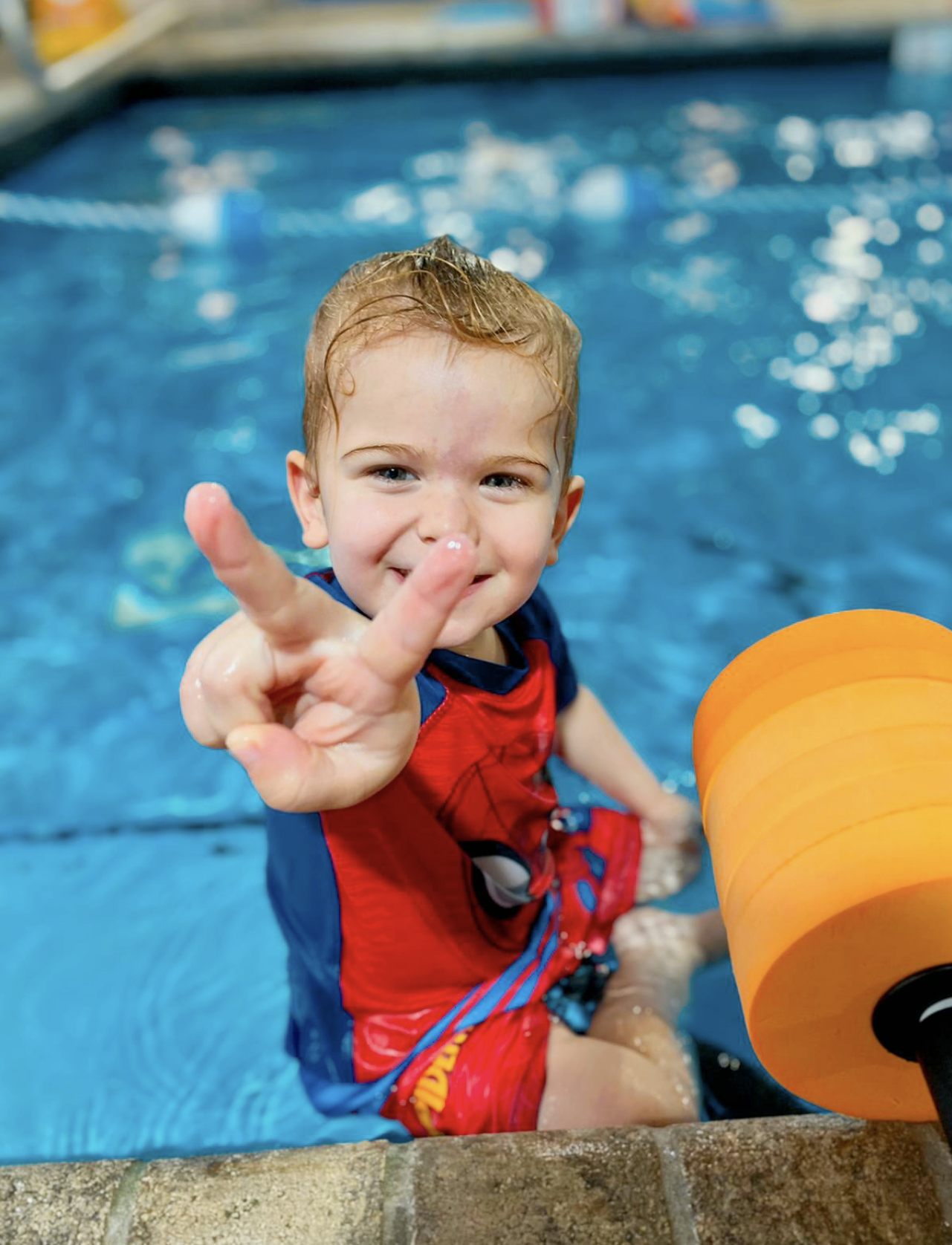 A young boy in the pool making a peace sign.