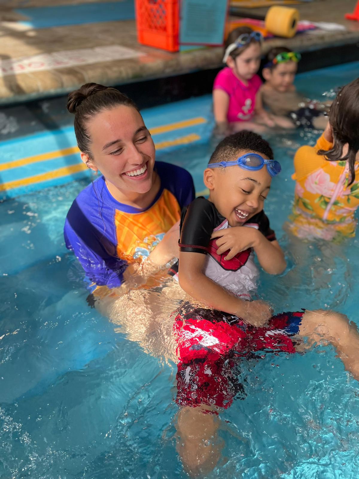 A woman and child in the pool with other children.