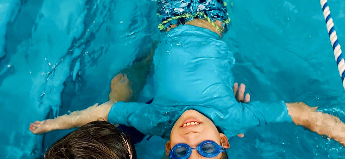 Two young boys in the pool with goggles on.