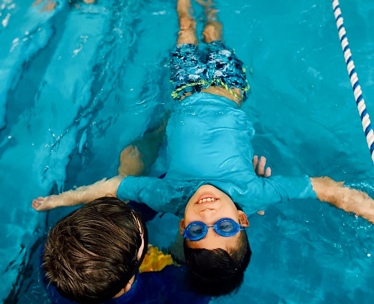 Two young boys in the pool with goggles on.
