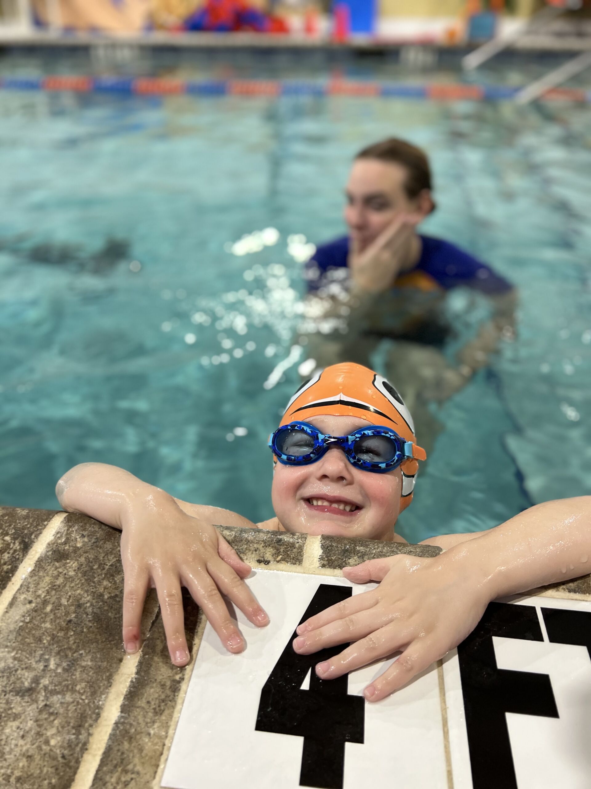 A young boy in the pool with his arms around another person.