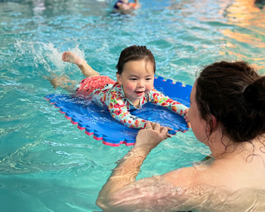 A baby is swimming in the water with an adult.