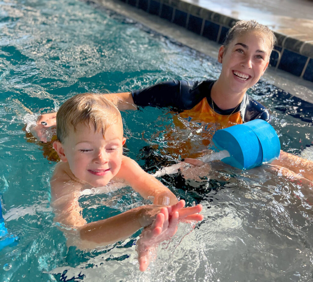 A boy and girl in the pool playing with water toys.